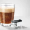 Glass of coffee with creamy foam next to a JURA syrup dispenser attachment.