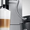 Close-up of a JURA coffee machine using a milk pipe with stainless steel casing to froth milk into a layered cappuccino or latte macchiato.