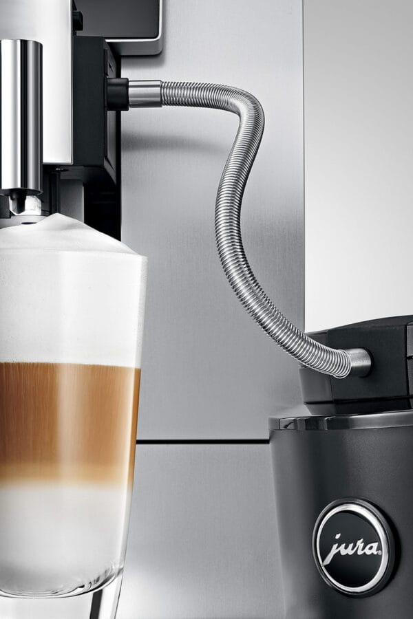 Close-up of a JURA coffee machine using a milk pipe with stainless steel casing to froth milk into a layered cappuccino or latte macchiato.