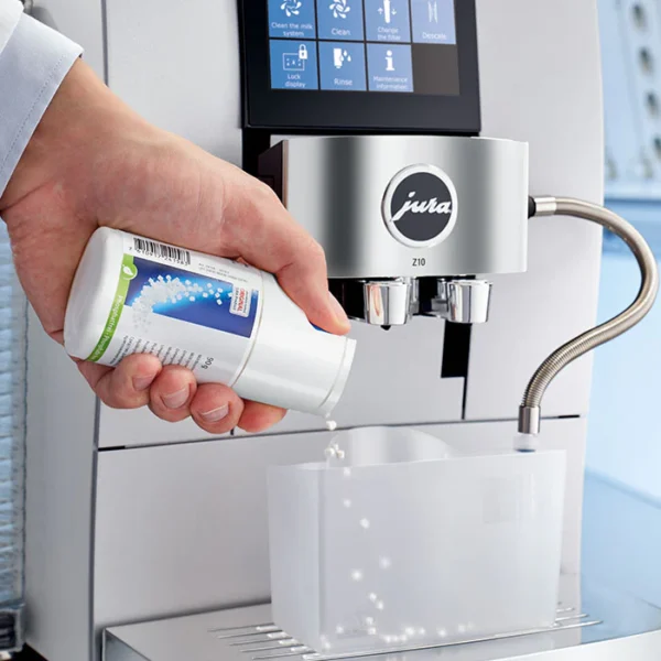 Hand dispensing JURA Milk System Cleaner Mini-Tabs 180 g into a JURA Z10 coffee machine for milk system cleaning.